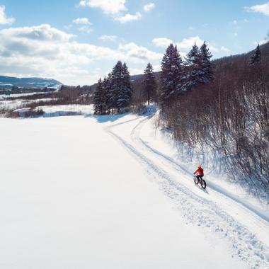 A person wearing a red jacket riding their bicycle up a snowy hill.
