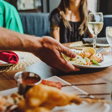 A server placing a seafood dish on a restaurant table with at least two guests.