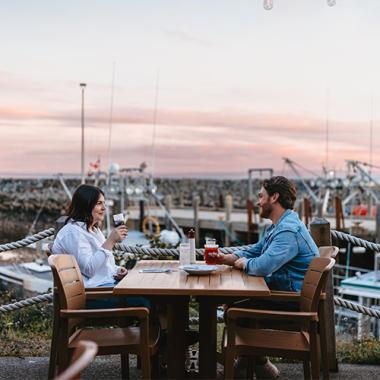 Two people sitting at a table at an eatery during sunset hours.