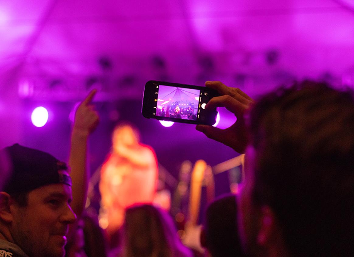 A person recording a musical performance on their phone during Harvest Music Festival